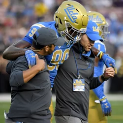 Sports medicine professionals helping an injured UCLA football player off the field 